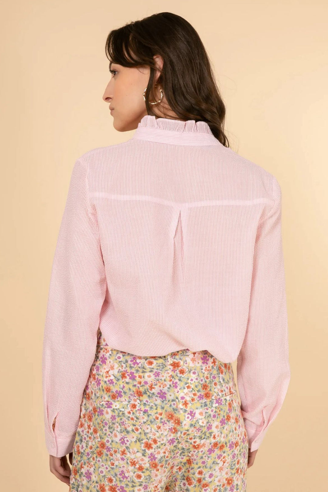 Woman wearing a light pink shirt and floral pants on a beige background