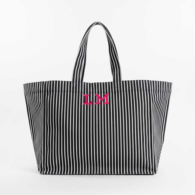 Black and white striped tote bag with pink initials on a light gray background