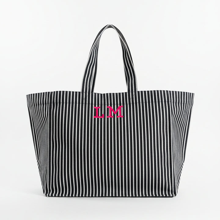 Black and white striped tote bag with pink initials on a light gray background