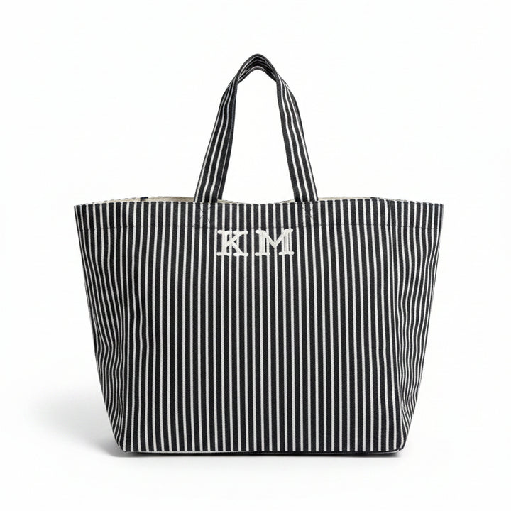 Black and white striped tote bag with 'KM' initials on a table in an indoor setting.