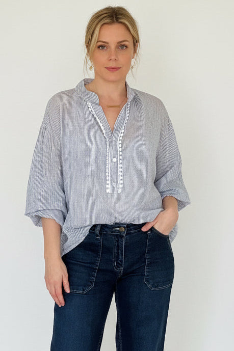 Person wearing a blue and white striped shirt with rolled-up sleeves and dark jeans against a white background.