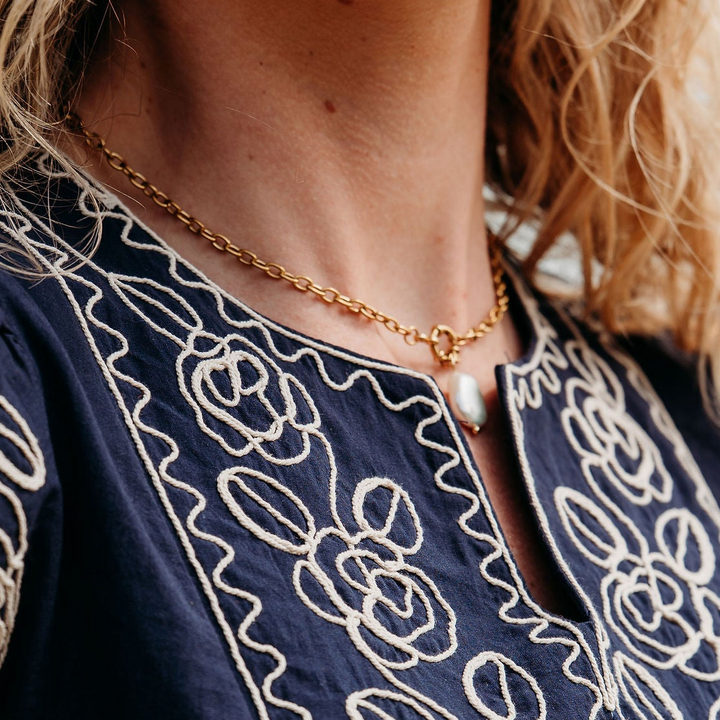 Woman wearing a navy blue dress with white embroidery, outdoors.