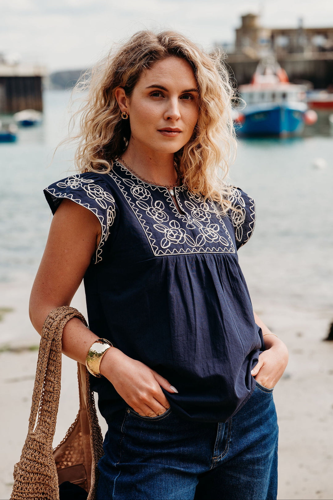 Woman wearing a navy blue top with white embroidery by a waterfront.