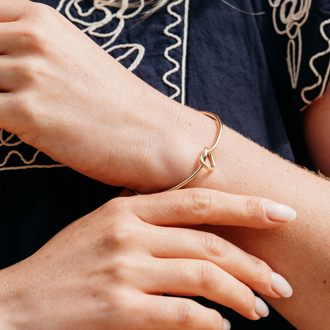 Person wearing a dark blue top with white embroidery, holding their arm.
