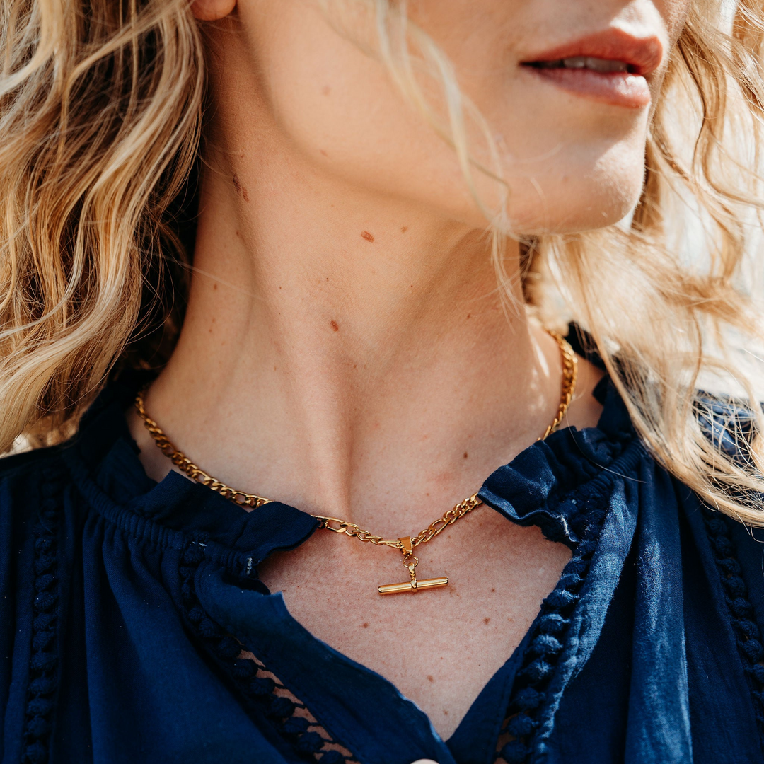Close-up of a person wearing a blue shirt and gold necklace with a small pendant.