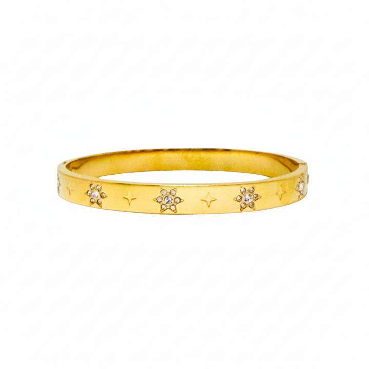 A gold bangle bracelet featuring a textured outer surface decorated with small star engravings and several flower motifs set with clear stones, shown against a plain white background.