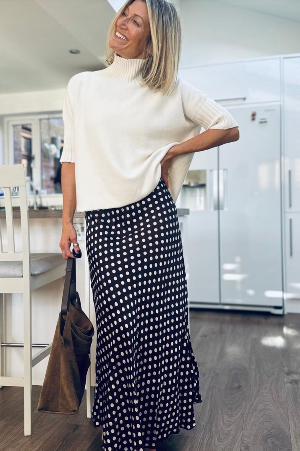 Woman wearing a white top and brown polka dot skirt in a kitchen.
