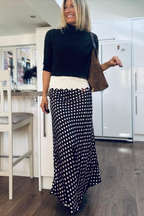 Woman in a kitchen wearing a black top and polka dot skirt.