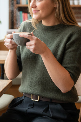 Person wearing a green alpaca sweater and black cord skirt 