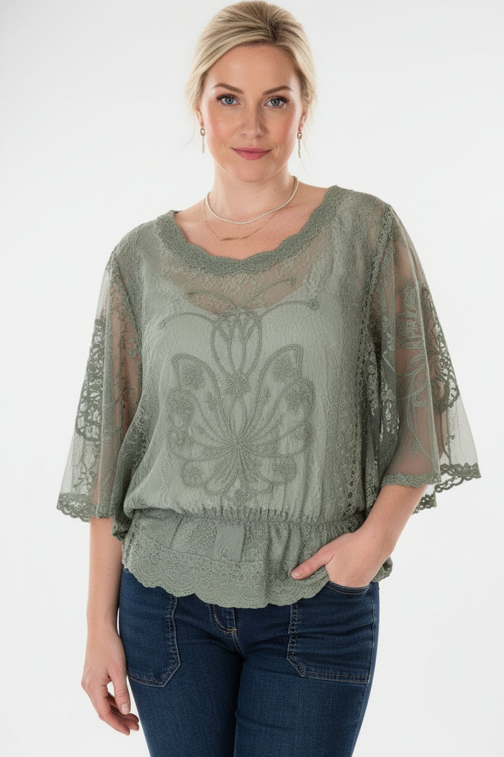 Woman wearing a green embroidered blouse with sheer sleeves against a neutral background