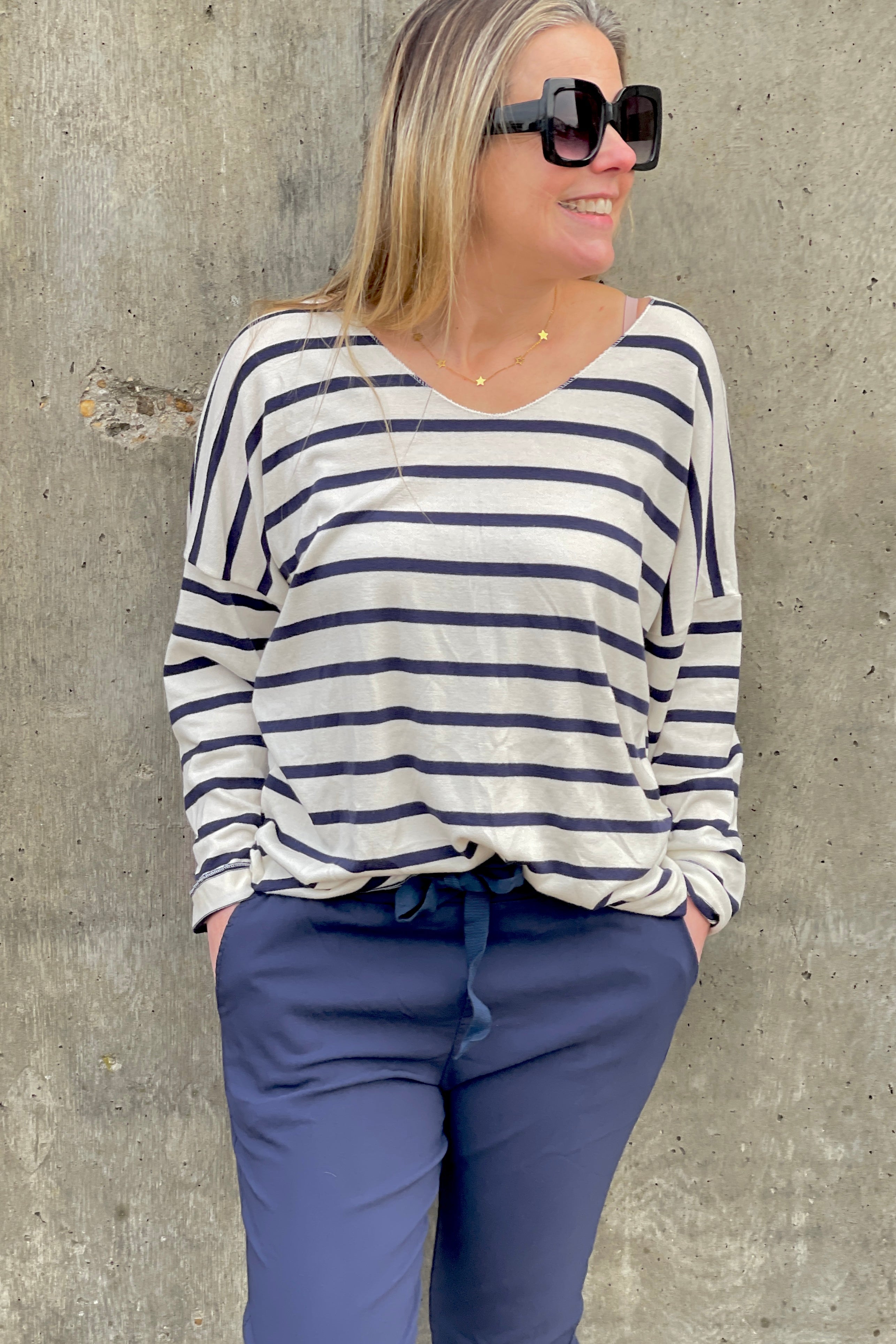 A woman wearing a navy and white striped long-sleeved top with a round neckline, paired with dark trousers.