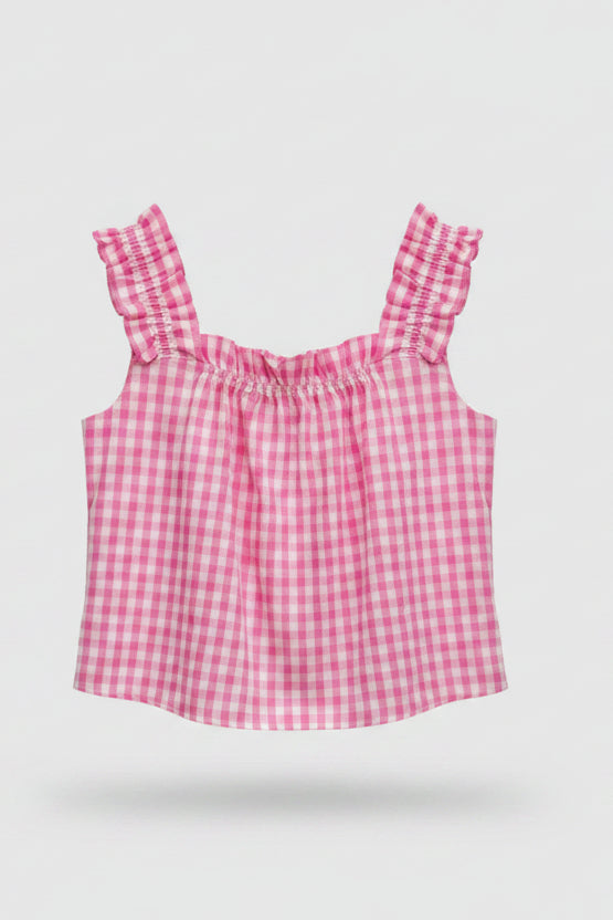 A pink and white gingham check sleeveless top with ruffled shoulder straps and a smocked bodice, hanging on a wooden hanger labeled 'APRIL NAVY' against a light fabric backdrop.