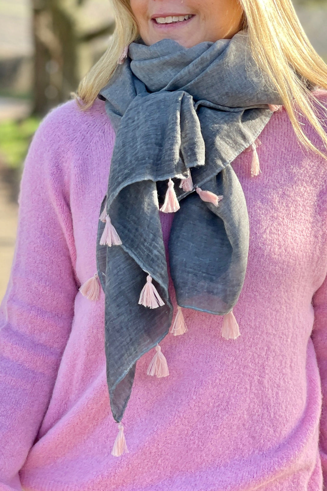 A person wearing a bright pink scarf with tassels, paired with a white t-shirt and blue denim shorts.