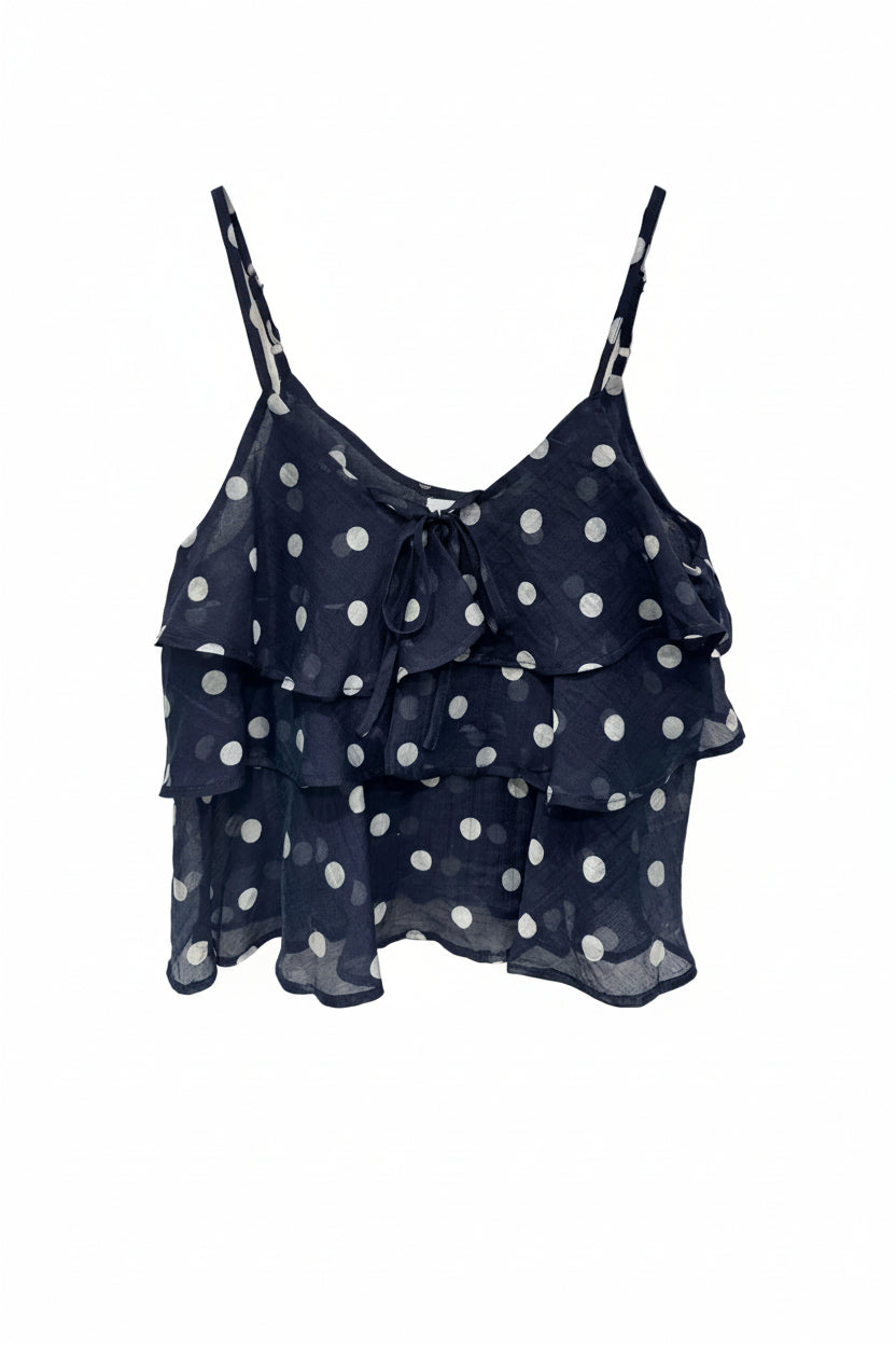 Navy blue top with white polka dots on a hanger against a white background
