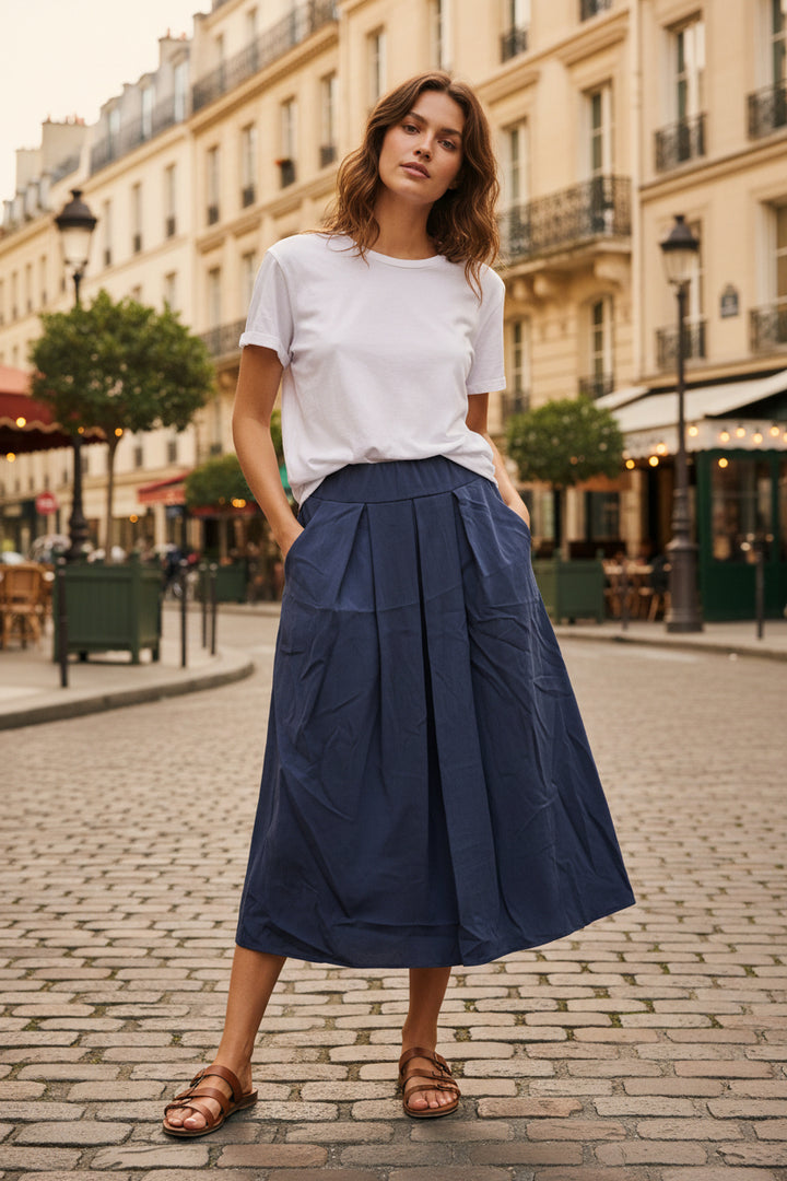 A dark slate blue pleated midi skirt hanging on a black hanger against a plain white background.