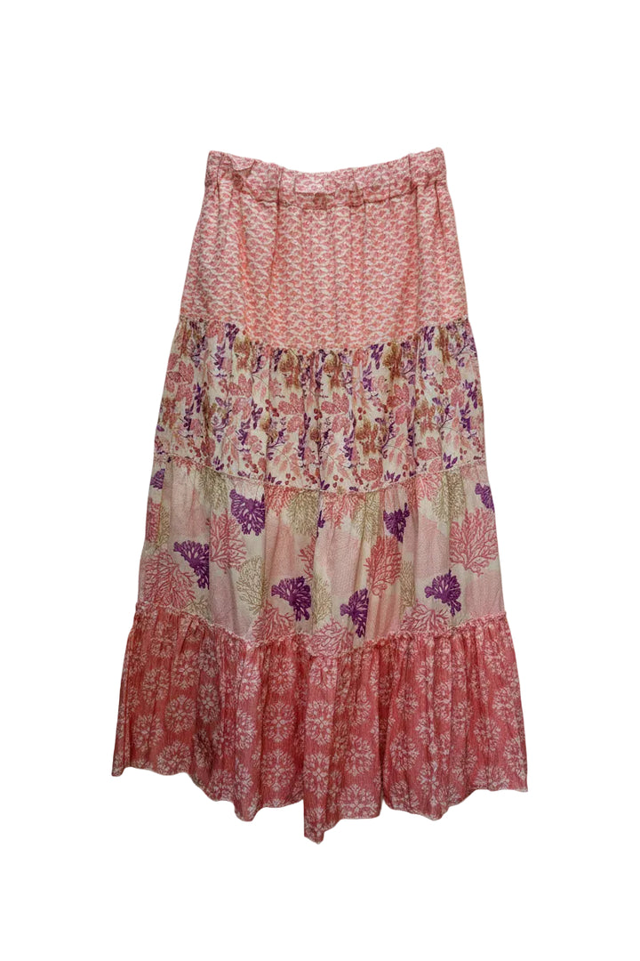 A tiered maxi skirt with a multicolor floral and paisley print in shades of pink, orange, purple, and beige, hanging on a wooden hanger against a plain white wall.