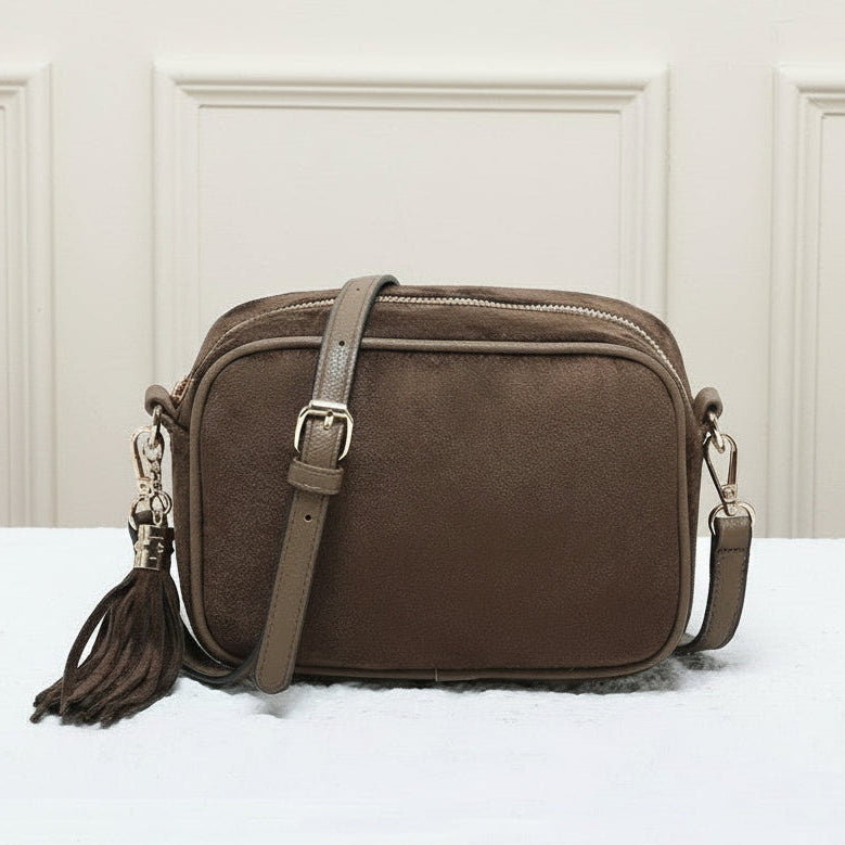 Brown leather crossbody bag with tassel on a white surface with a beige paneled wall background