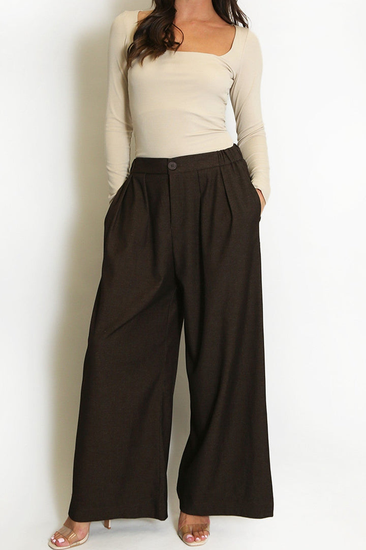 Woman wearing a beige top and brown wide-leg pants against a white background